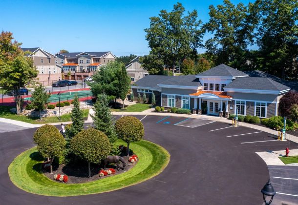 Aerial view of The Lofts at Saratoga clubhouse, landscaped roundabout, tennis court, and apartments in Malta, NY.