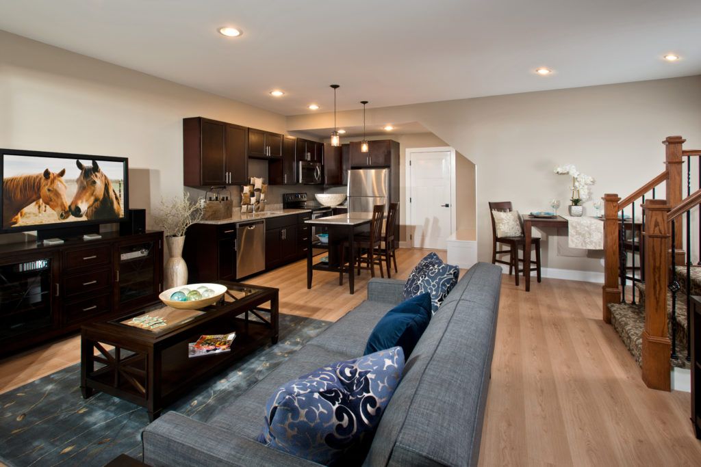 Lofts at Saratoga living room with a grey couch, situated next to a kitchen with stainless steel appliances and brown cabinets.
