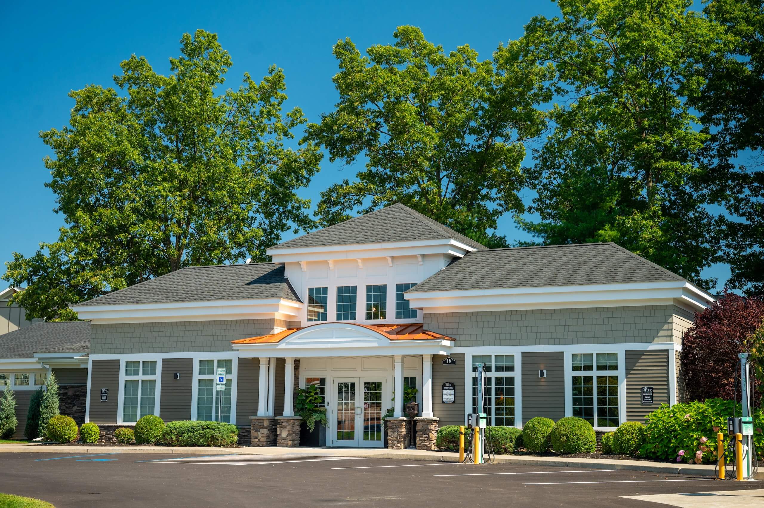 Exterior view of The Lofts at Saratoga Blvd featuring a parking lot and large trees in Malta, NY.