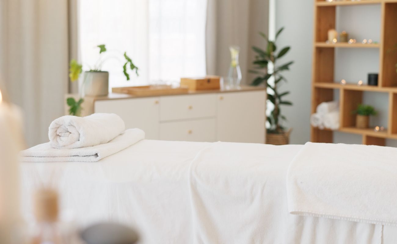 Spa, massage bed and background with candles and empty room for health, wellness and treatment. Physical therapy table, luxury resort or beauty salon for body care, relax or peace